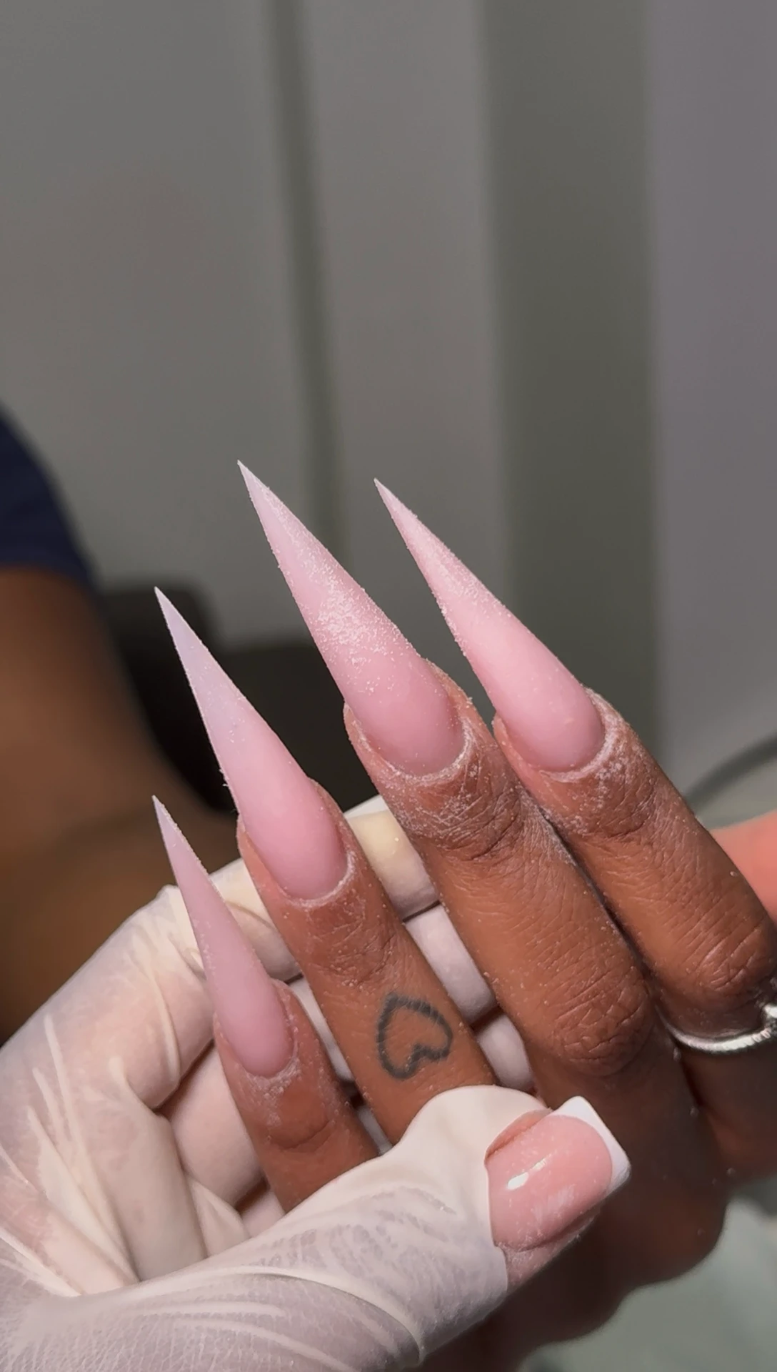 Long pink stiletto nails held by a technician in a white glove